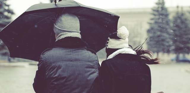 man and woman wearing winter coats and hats and walking under an umbrella