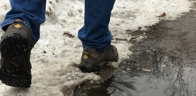 person wearing hiking shoes walking beside a slushy puddle